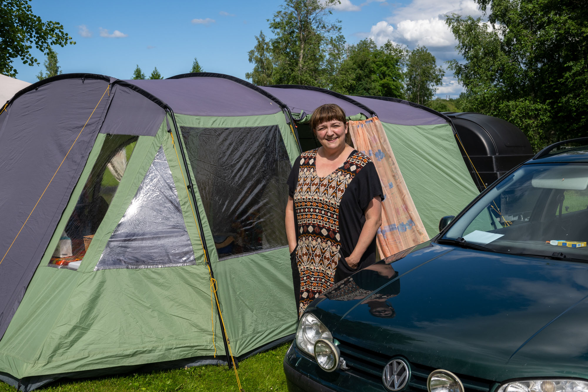 Nainen seisoo teltan ja auton välissä.