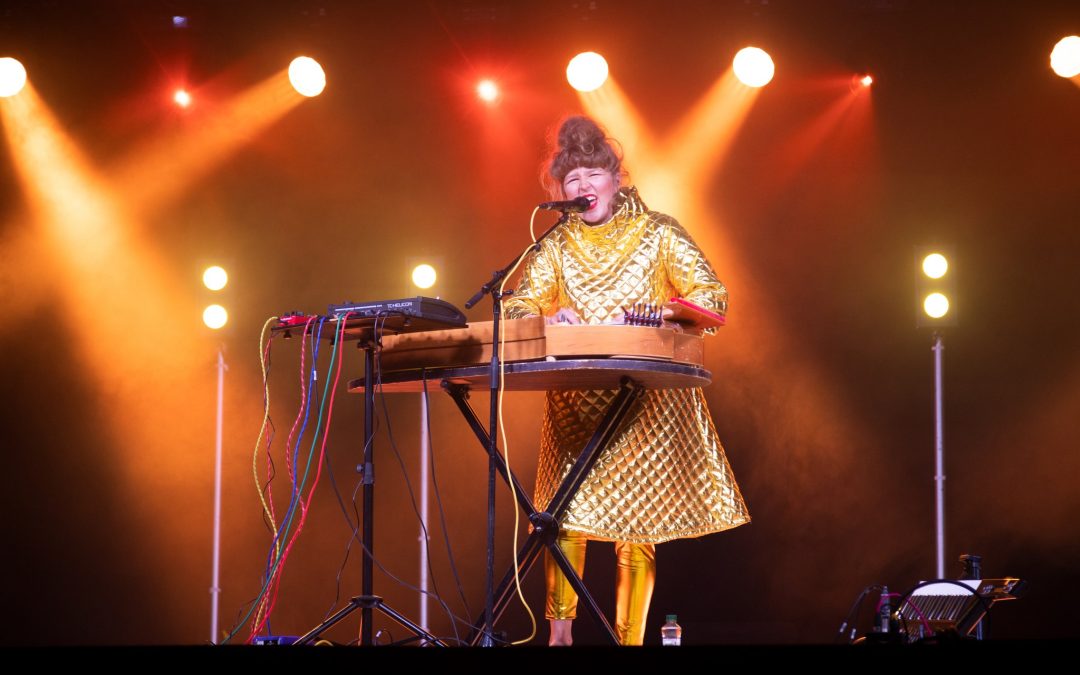Pelkkä Poutanen -niminen artisti esiintyy festivaalilavalla seisten soittimenaan konserttikantele. Lava on valaistu ja esiintyjällä on kultaiset vaatteet, jonka vuoksi kuva on häikäisevä.