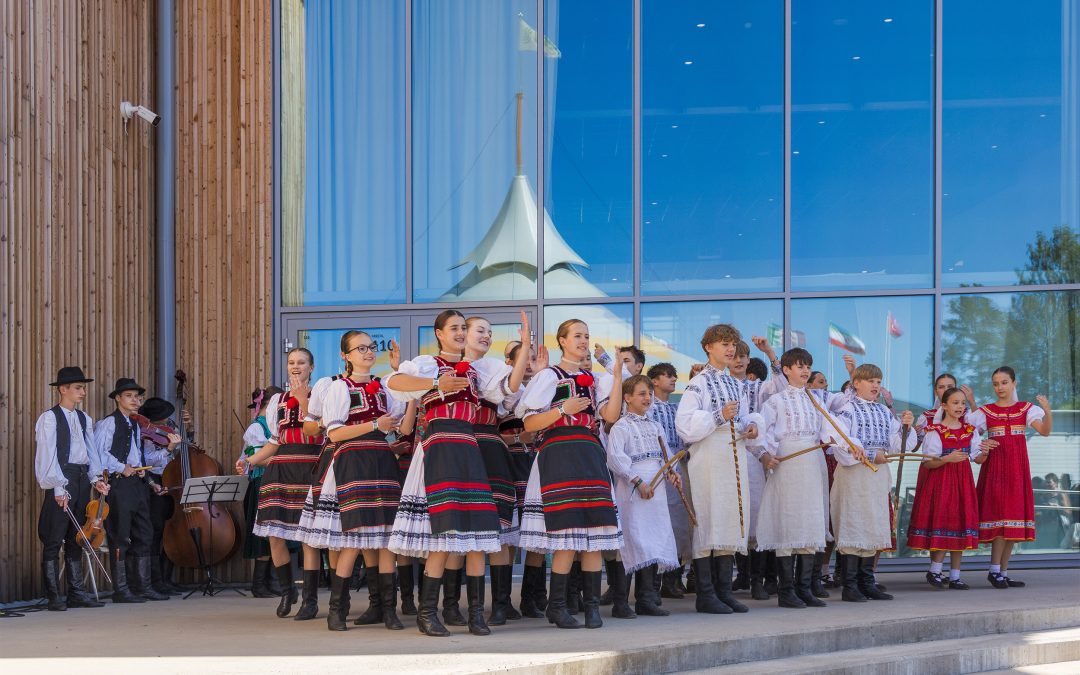 Iso ryhmä ulkolavalla, lasiseinä peilaa taivasta.